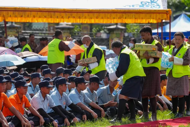 Volunteers distributing water and supplies to seated schoolchildren at a community event